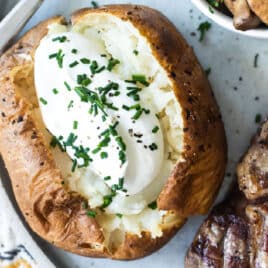 A plate with a baked potato topped with sour cream, a steak topped with butter, and a bowl of balsamic mushrooms on a plate.