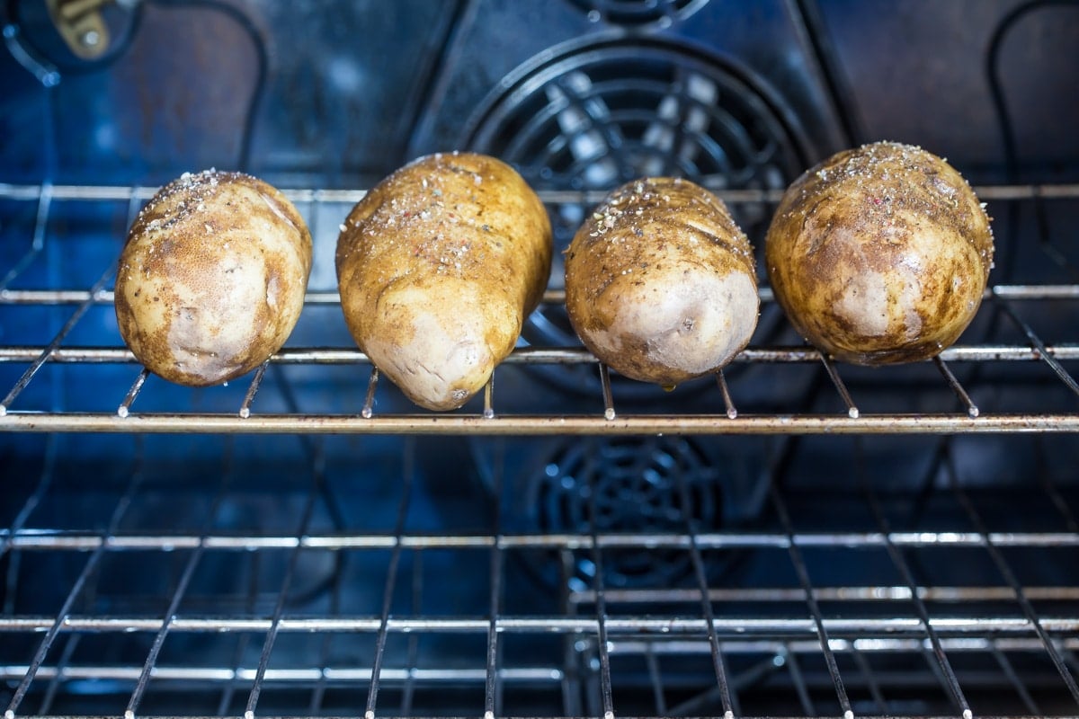 4 potatoes on an oven rack in the oven.