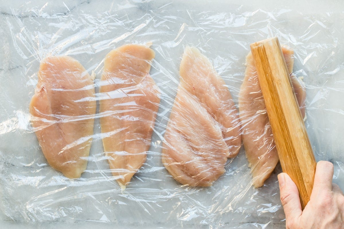 Pounding chicken cutlets thin under plastic wrap.