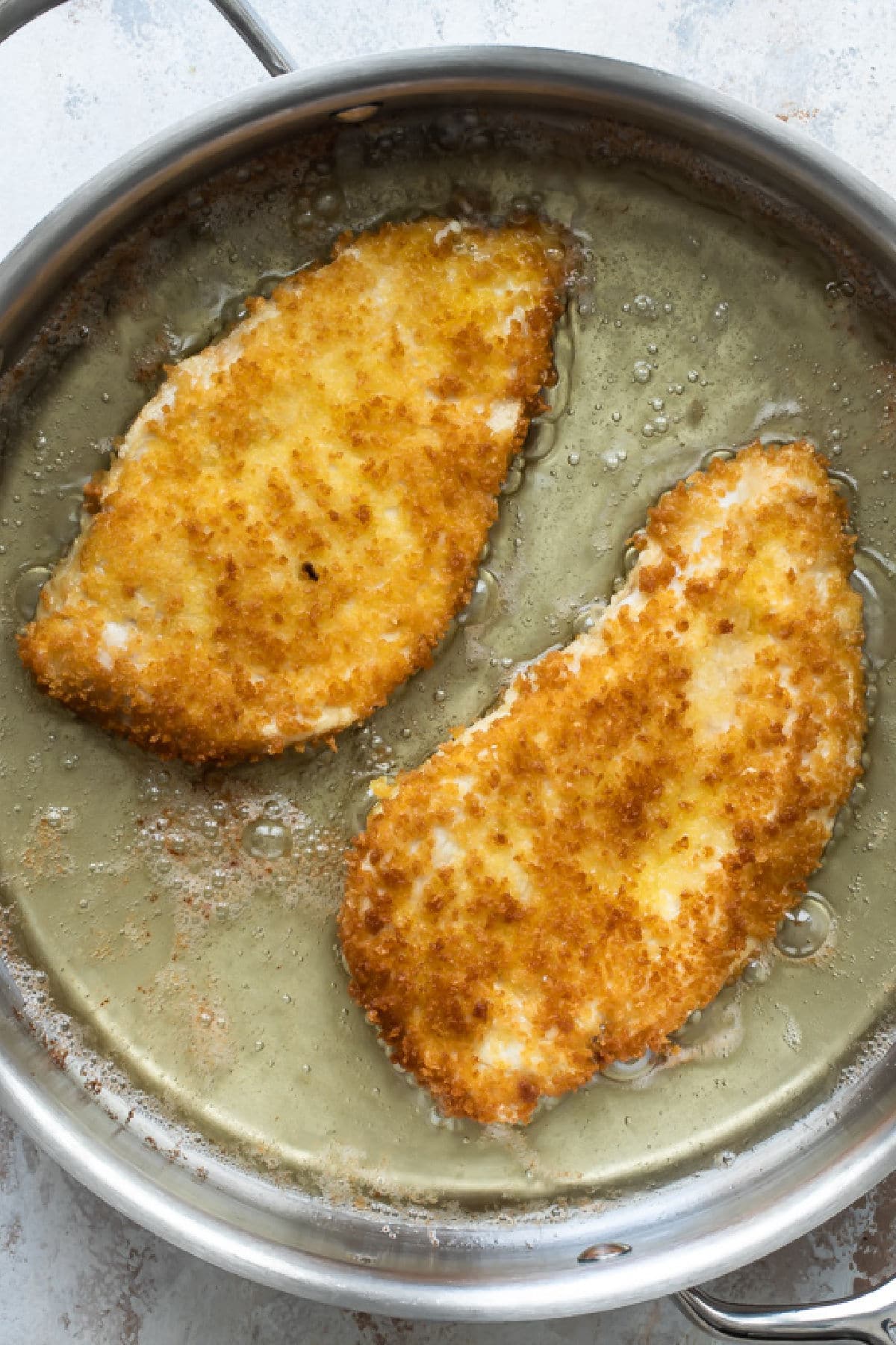 Chicken cutlets frying in oil in a skillet.