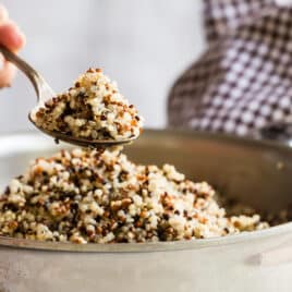 Cooked quinoa in a sliver bowl with someone spooning some out.