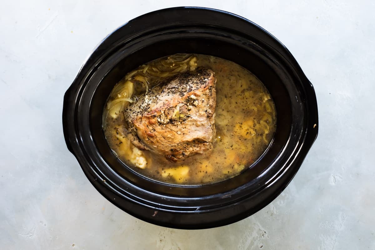 A browned beef roast in a slow cooker with pickled vegetables.