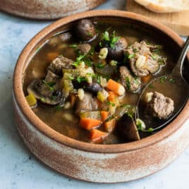 Slow cooker beef barley soup in a brown bowl.