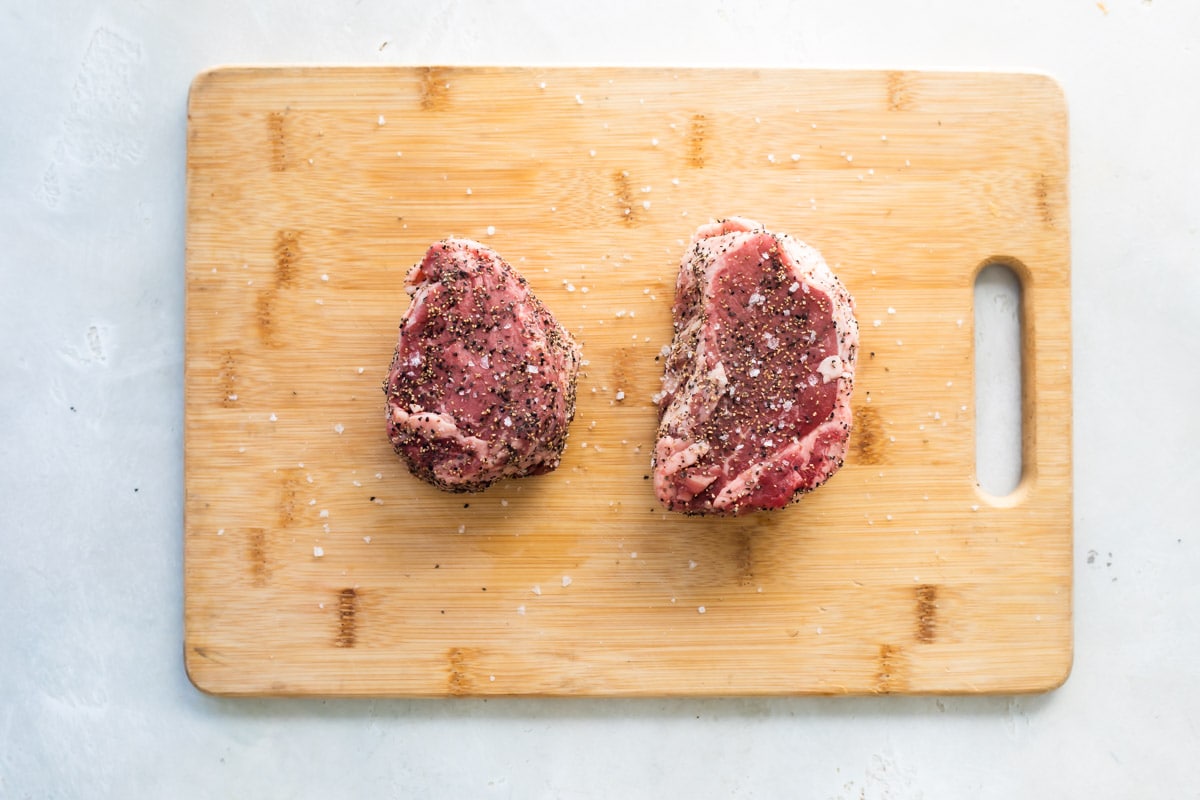 Two seasoned filet mignons on a cutting board.