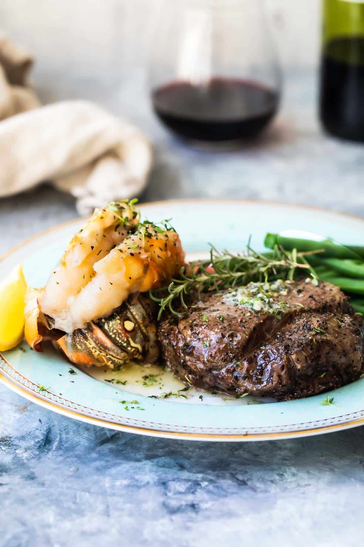 Surf and Turf (a filet mignon with a lobster tail) on a white plate with wine in the background.