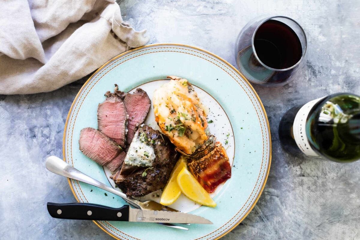 Surf and Turf (a filet mignon with a lobster tail) on a white plate with wine in the background.