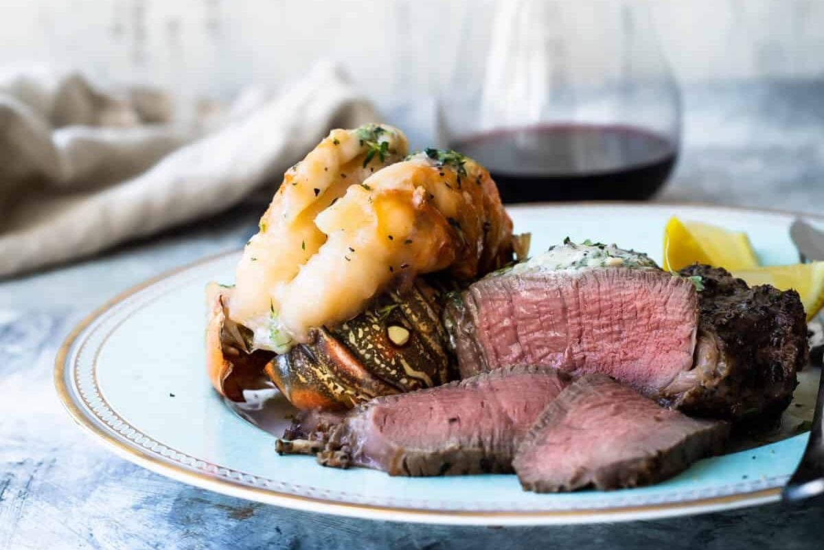 Surf and Turf (a filet mignon with a lobster tail) on a white plate with wine in the background.