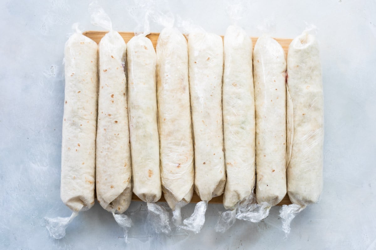 A board full of turkey roll ups wrapped in plastic.