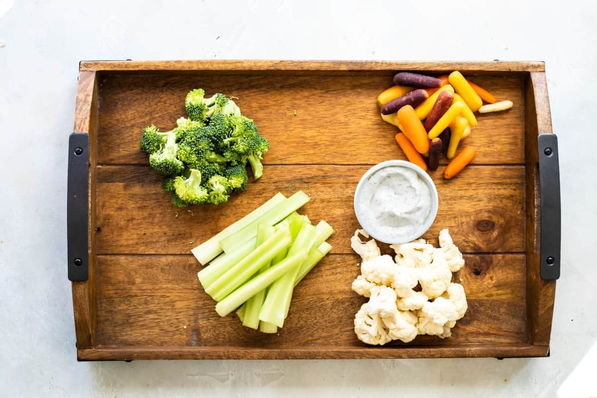 A platter full of fresh vegetables with a bowl of veggie dip.