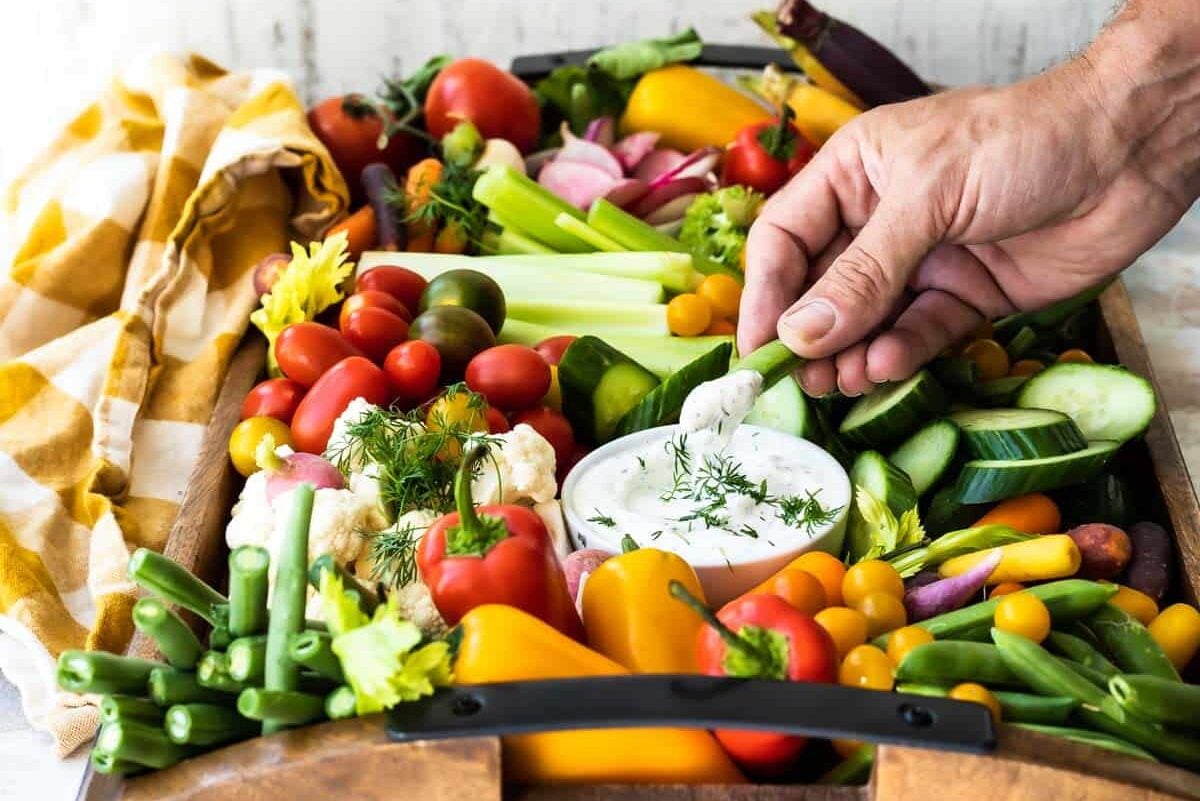 A platter full of fresh vegetables with a bowl of veggie dip.