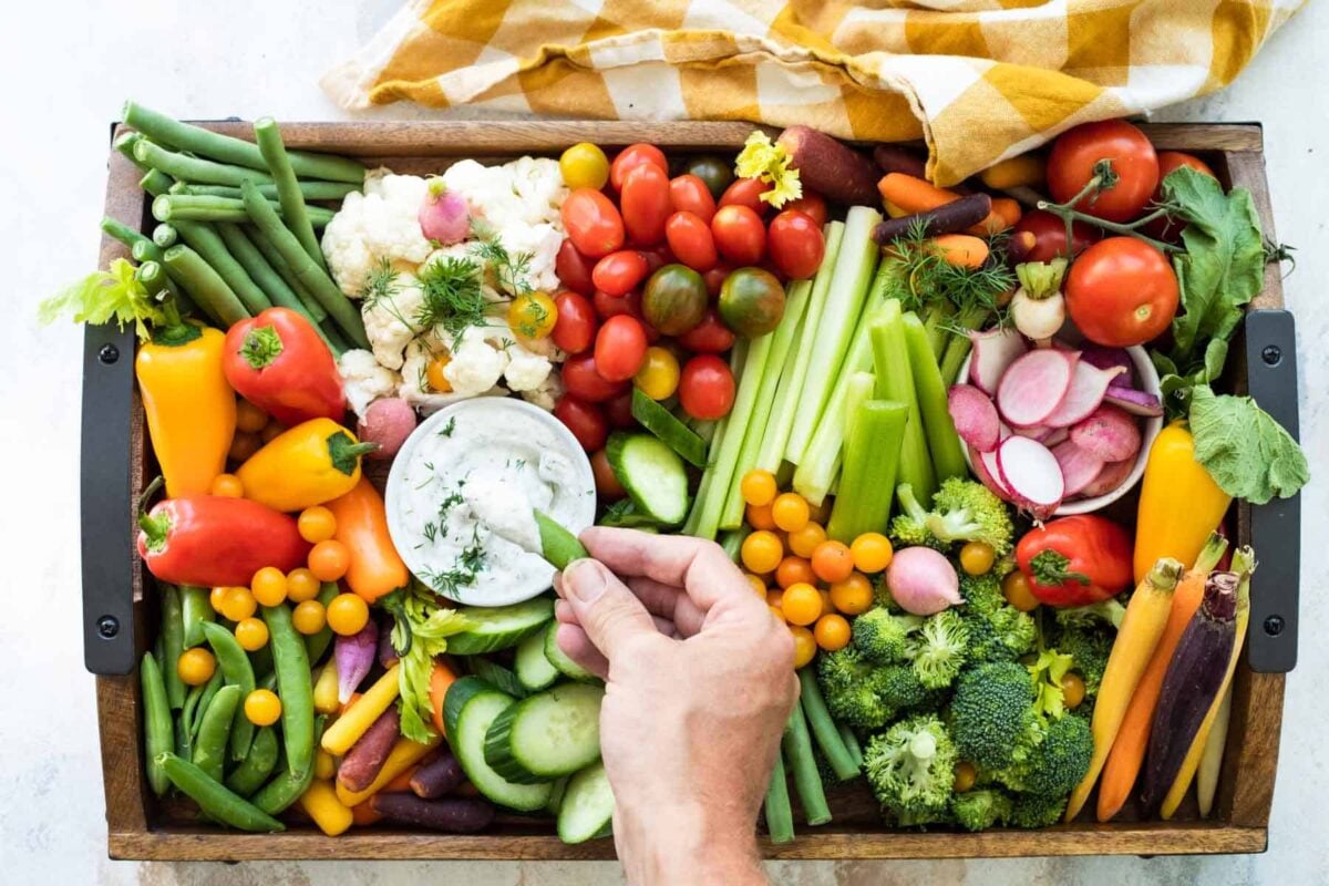 Someone dipping a vegetable into dill dip on a veggie platter.