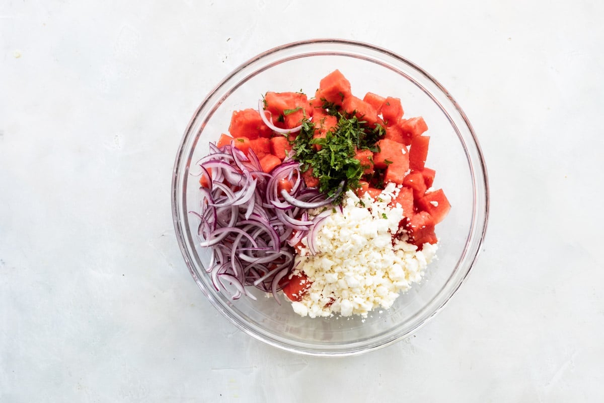 Assembling a watermelon salad in a glass bowl.
