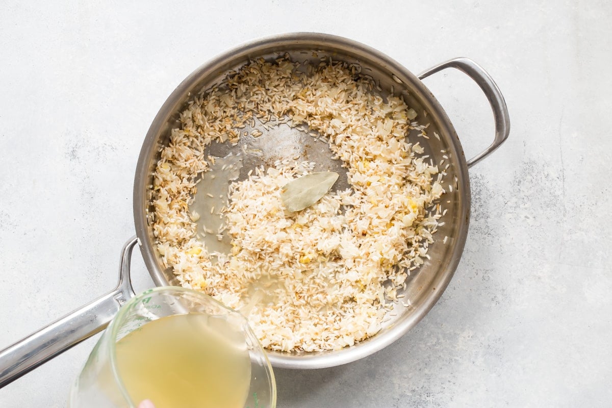 Broth being added to lemon rice in a silver skillet.