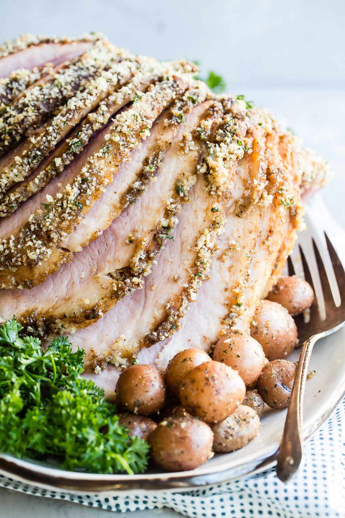 A platter of baked ham with roasted potatoes.