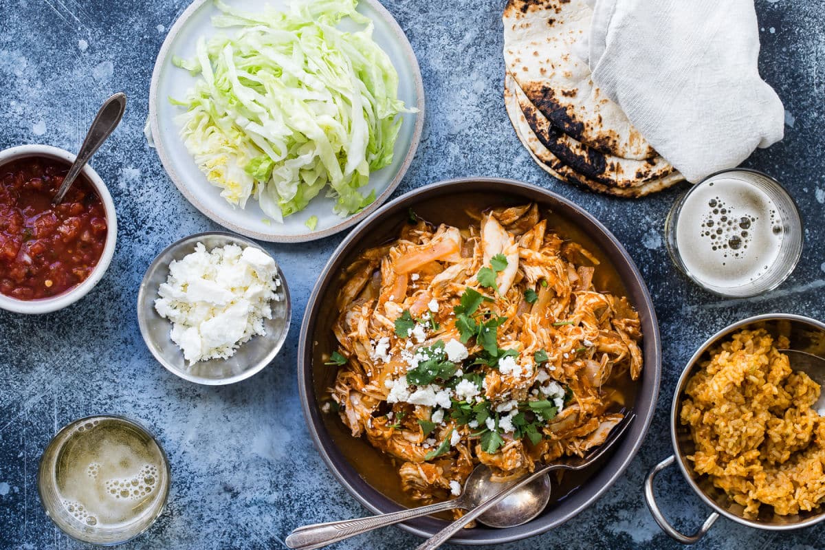 Chicken tinga in a bowl with tortilla shells and lettuce nearby.