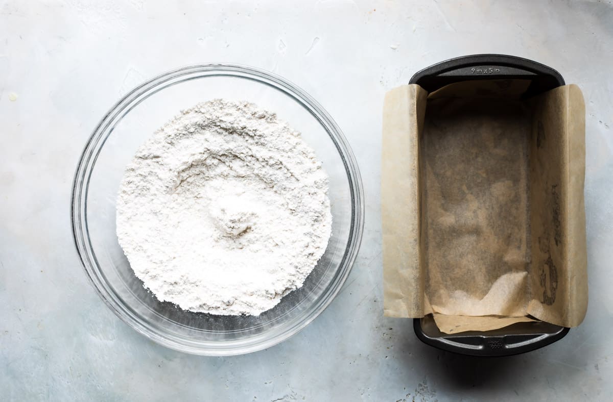 A bowl of flour next to a lined bread pan.