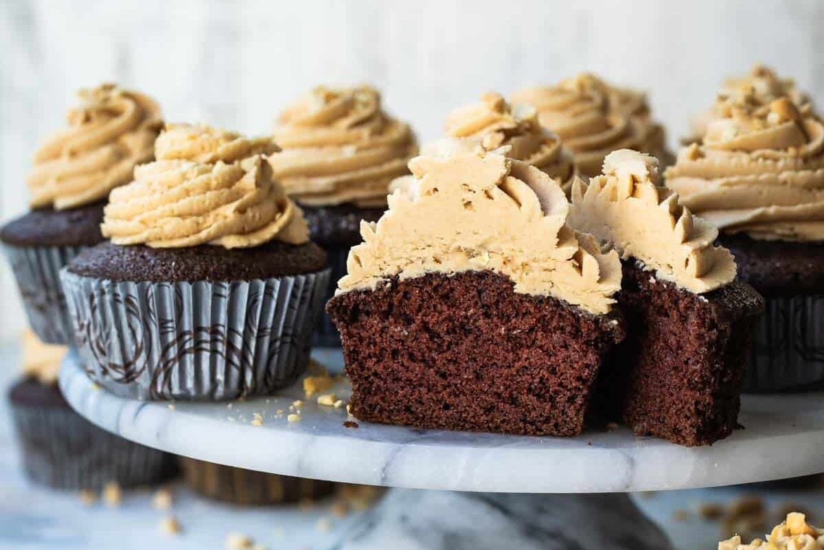 A cake stand filled with chocolate cupcakes with peanut butter frosting, 1 cut open to show the inside.