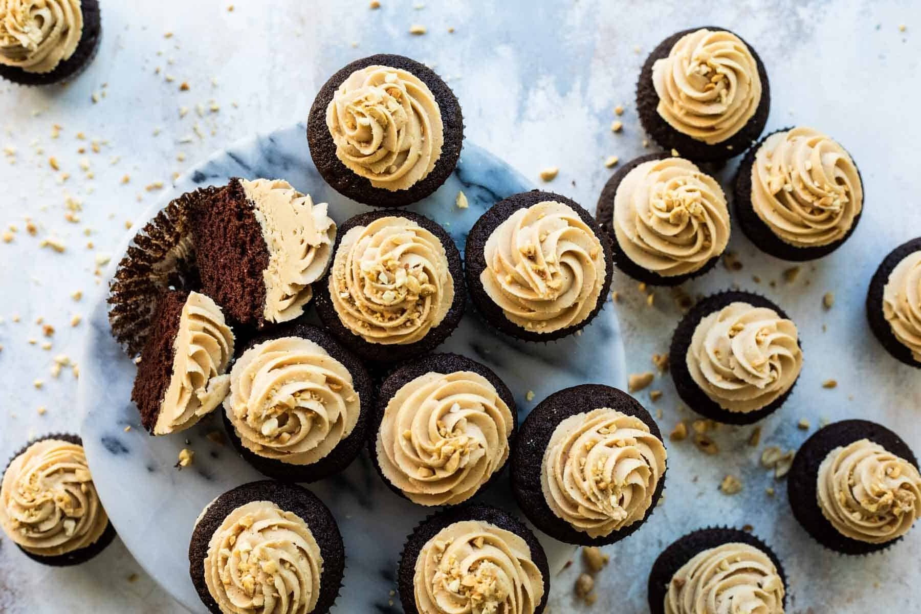 A plate filled with chocolate cupcakes with peanut butter frosting, 1 cut open to show the inside.