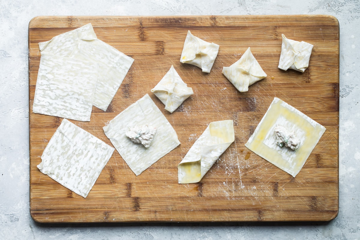 Cream cheese wontons being assembled on a wooden cutting board.