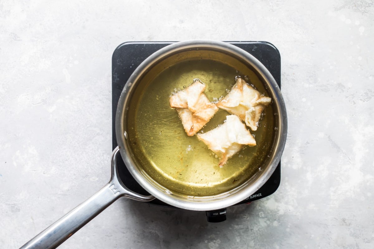 Cream cheese wontons being fried in oil.