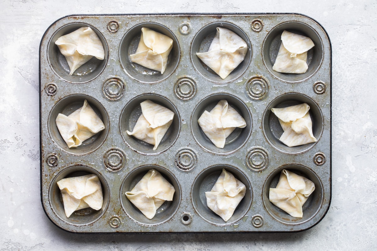 Cream cheese wontons in a muffin pan before being baked.