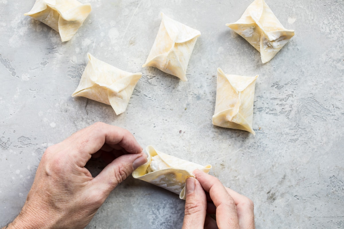 Someone assembling cream cheese wontons.