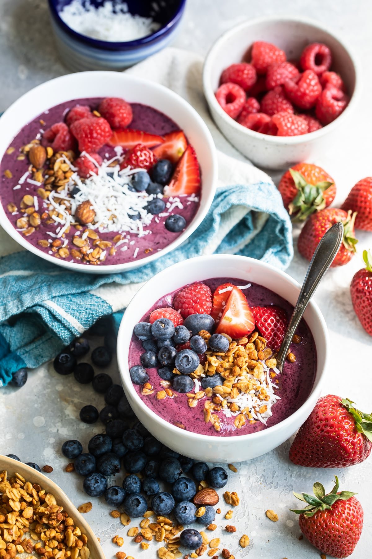 Two easy acai bowls surrounded by berries on a counter.