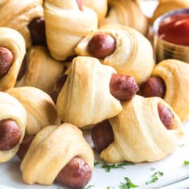 Easy pigs in a blanket on a white plate with a side of ketchup.