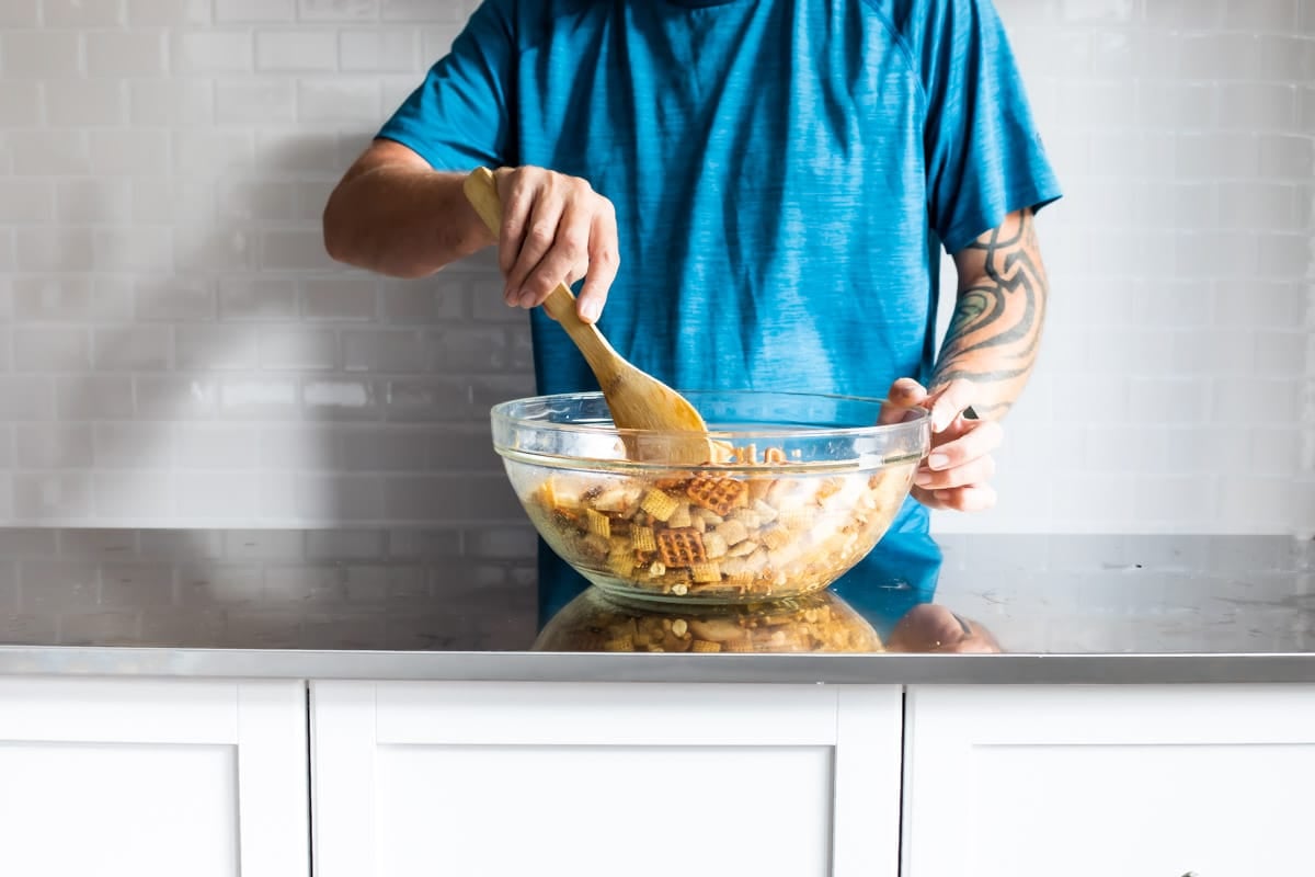 Someone stirring a bowl of Chex mix.