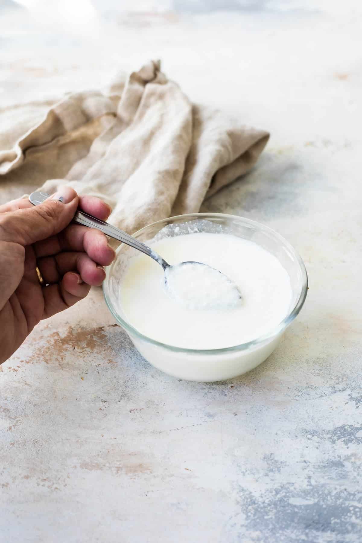 Someone spooning buttermilk out of a small clear bowl.