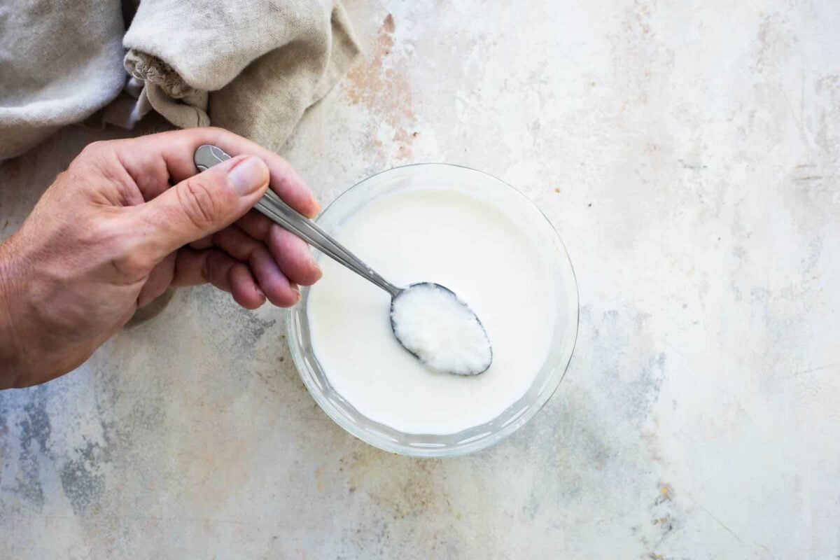Someone spooning buttermilk out of a small clear bowl.