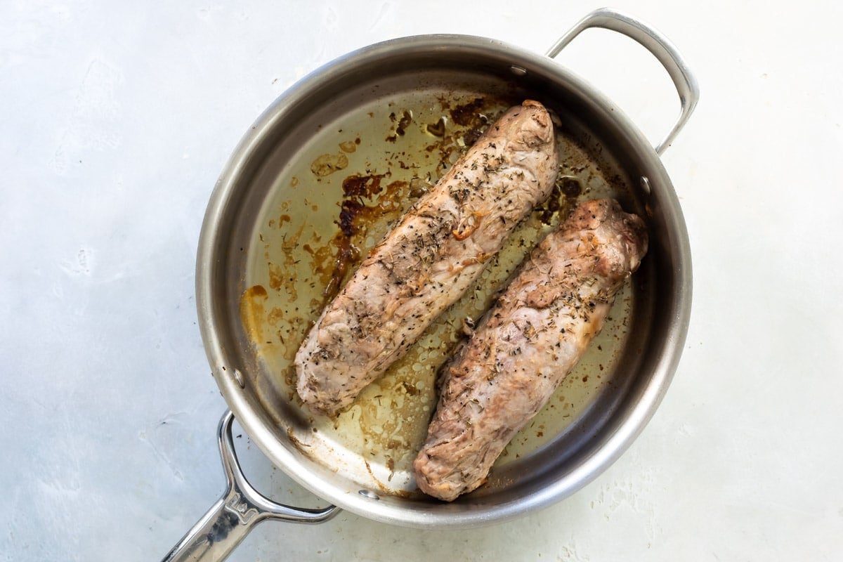 Pork tenderloin being cooked in a silver skillet.
