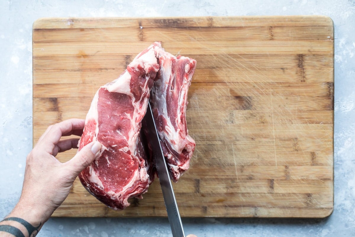 Raw prime rib being sliced on a wooden cutting board.