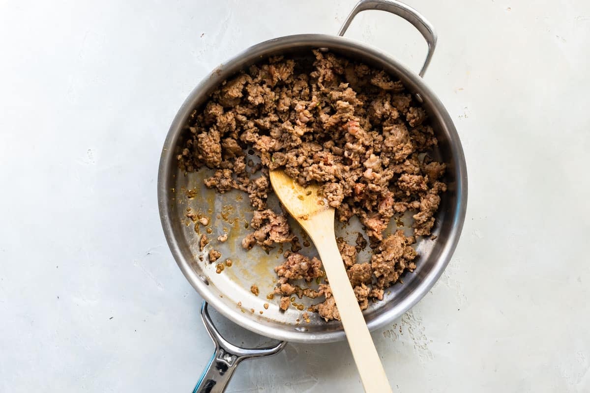 Italian sausage cooking in a large skillet.
