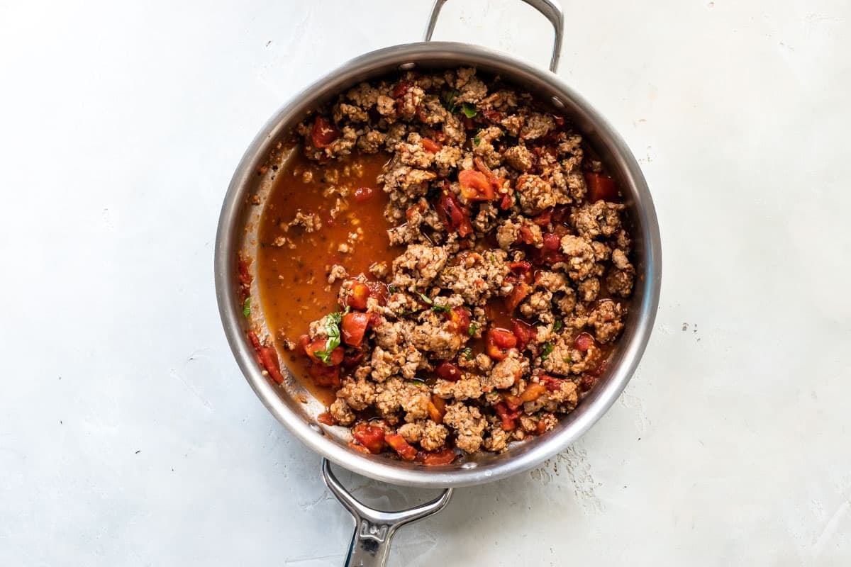 Italian sausage in a skillet with diced tomatoes.