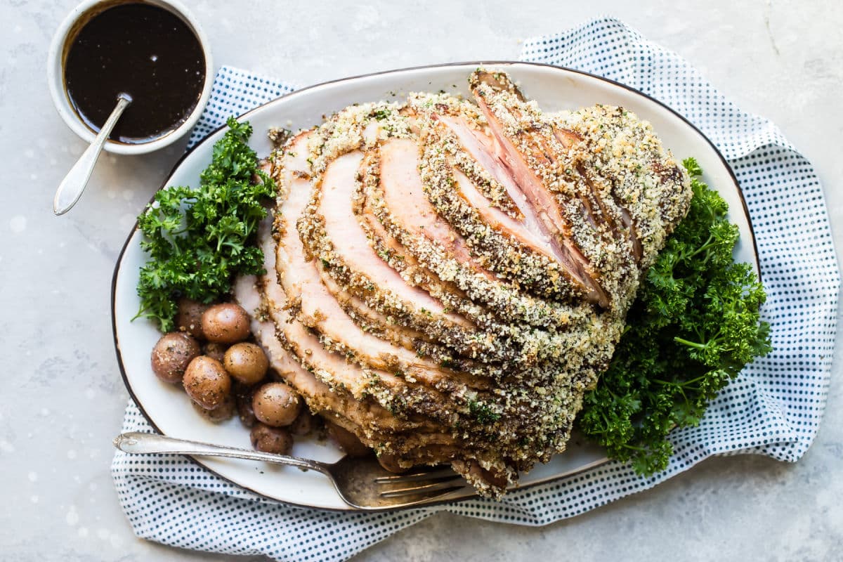 A platter of baked ham with roasted potatoes.