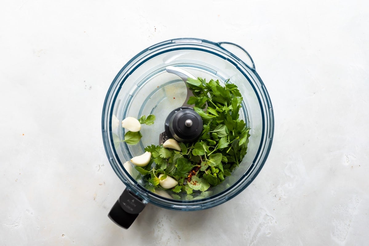 Chimichurri sauce ingredients in a food processor before being blended.