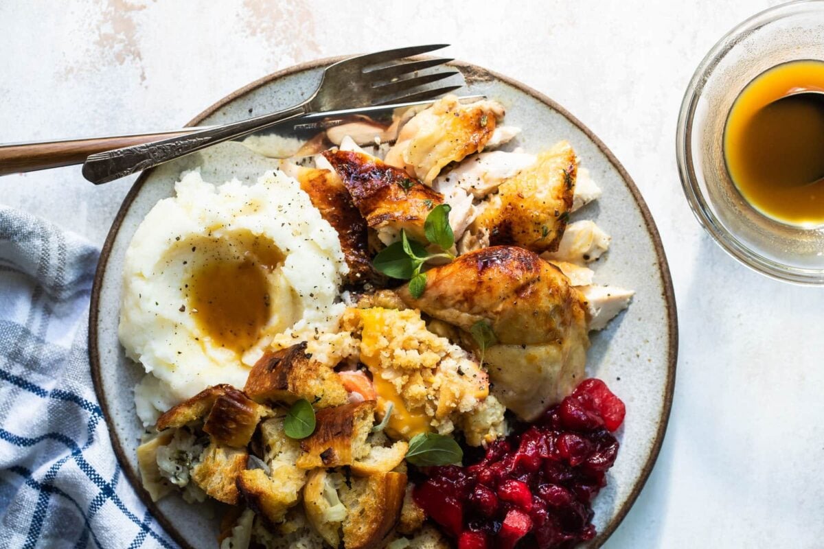 A carved Cornish hen on a gray plate with mashed potatoes, stuffing, and cranberry sauce.