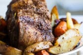 A pork roast on a white plate next to vegetables.