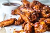 Air fryer chicken wings covered in barbecue sauce on a wooden cutting board.