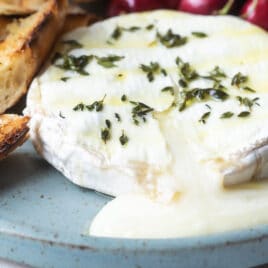 Baked brie on a blue plate with cherries and toasted bread pieces.