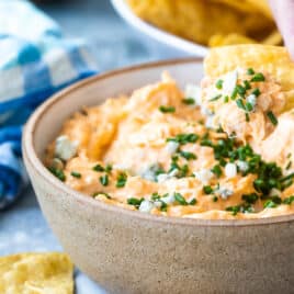 Someone dipping a tortilla chip in buffalo chicken dip.