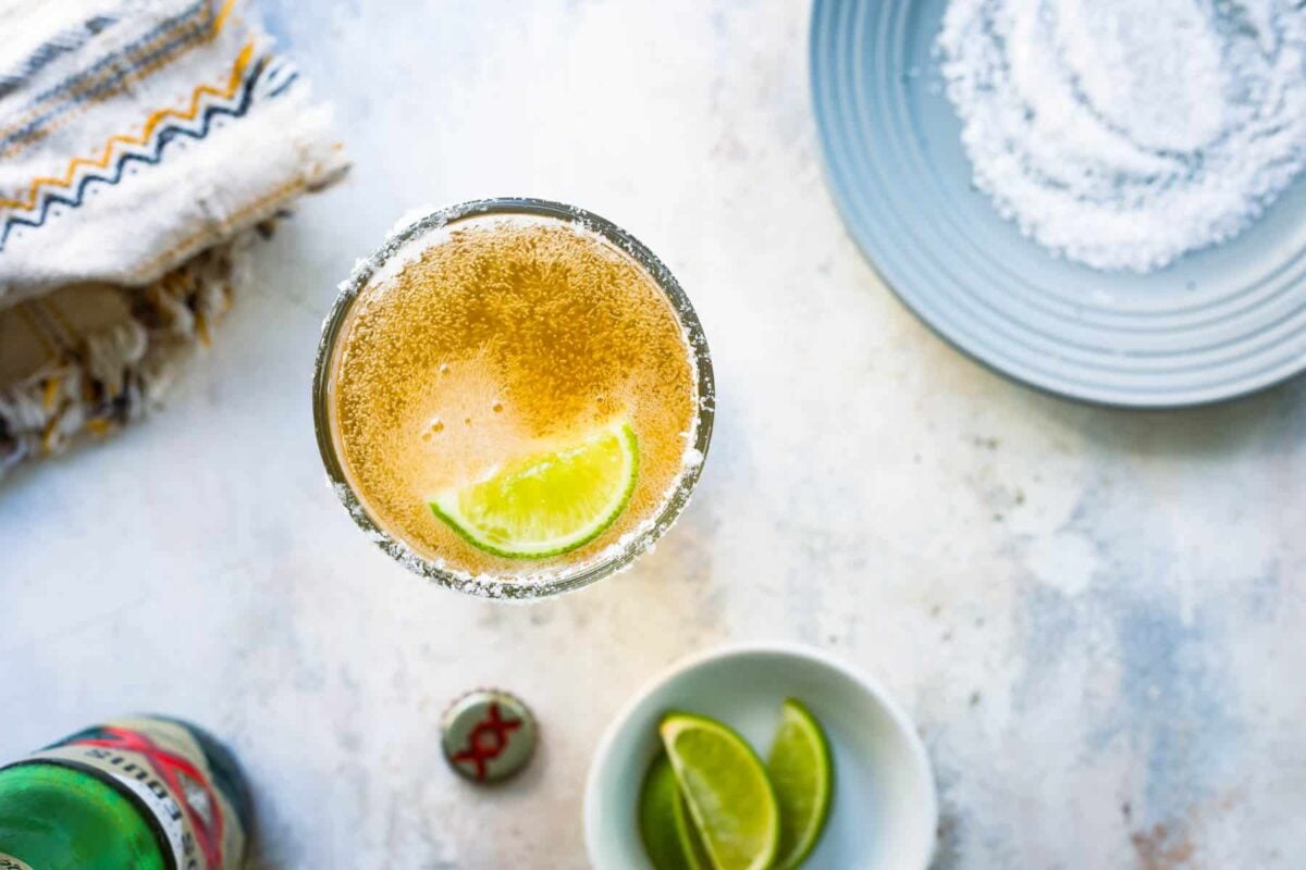 A chelada next to a plate of salt and a bowl of limes.