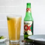 A Chelada next to a beer bottle and a small bowl of limes.