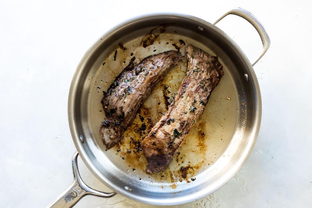 Chimichurri steak being cooked in a silver skillet.