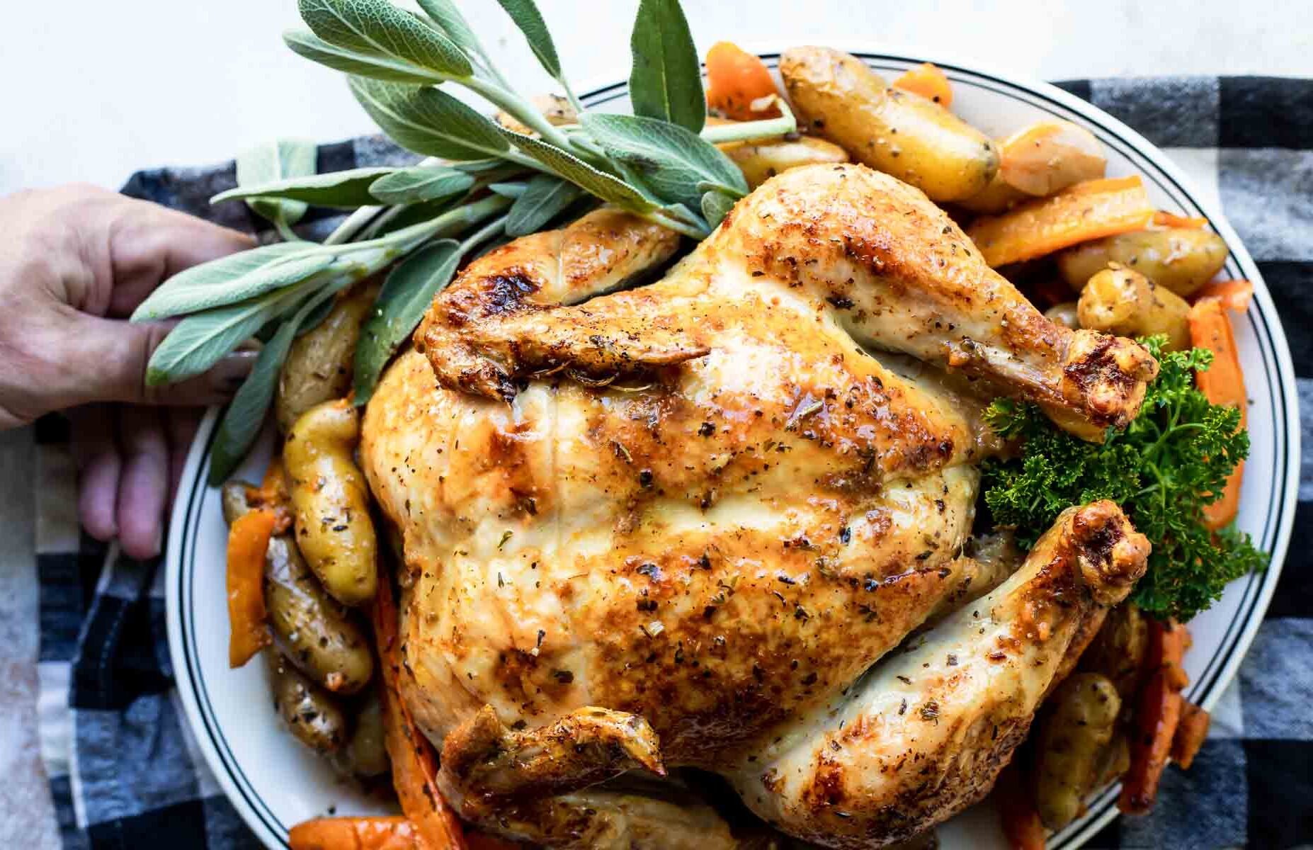 A whole garlic butter roasted chicken and vegetables on a white plate.
