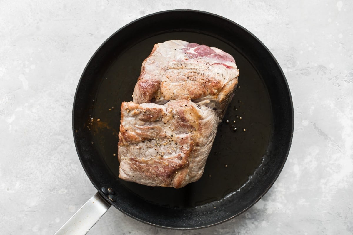 A slab of pork cooking in a black skillet.