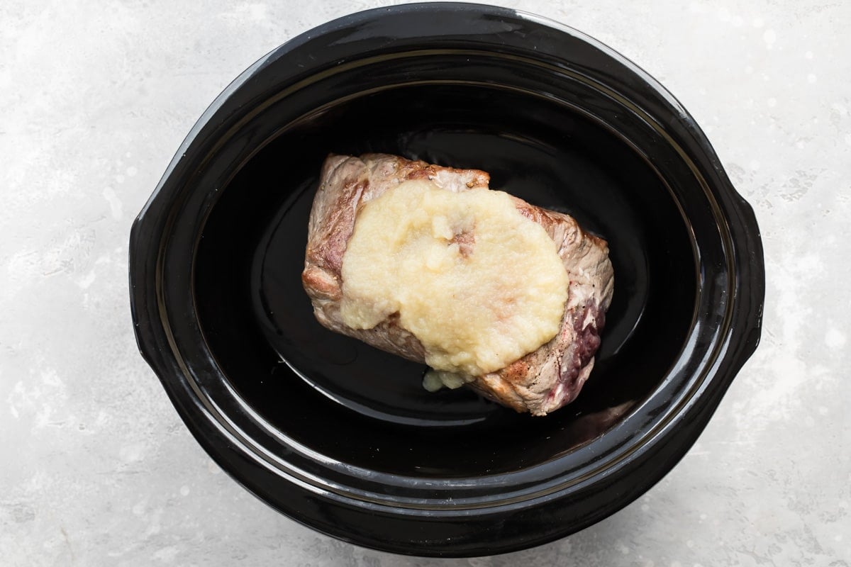 A slab of pork in a black slow cooker.