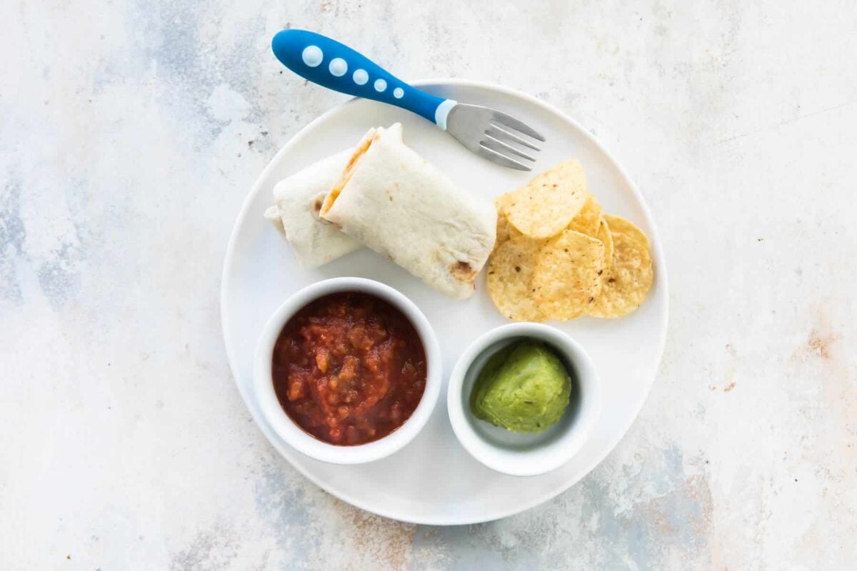 A toddler lunch of a quesadilla with a side of chips, salsa, and avocado.