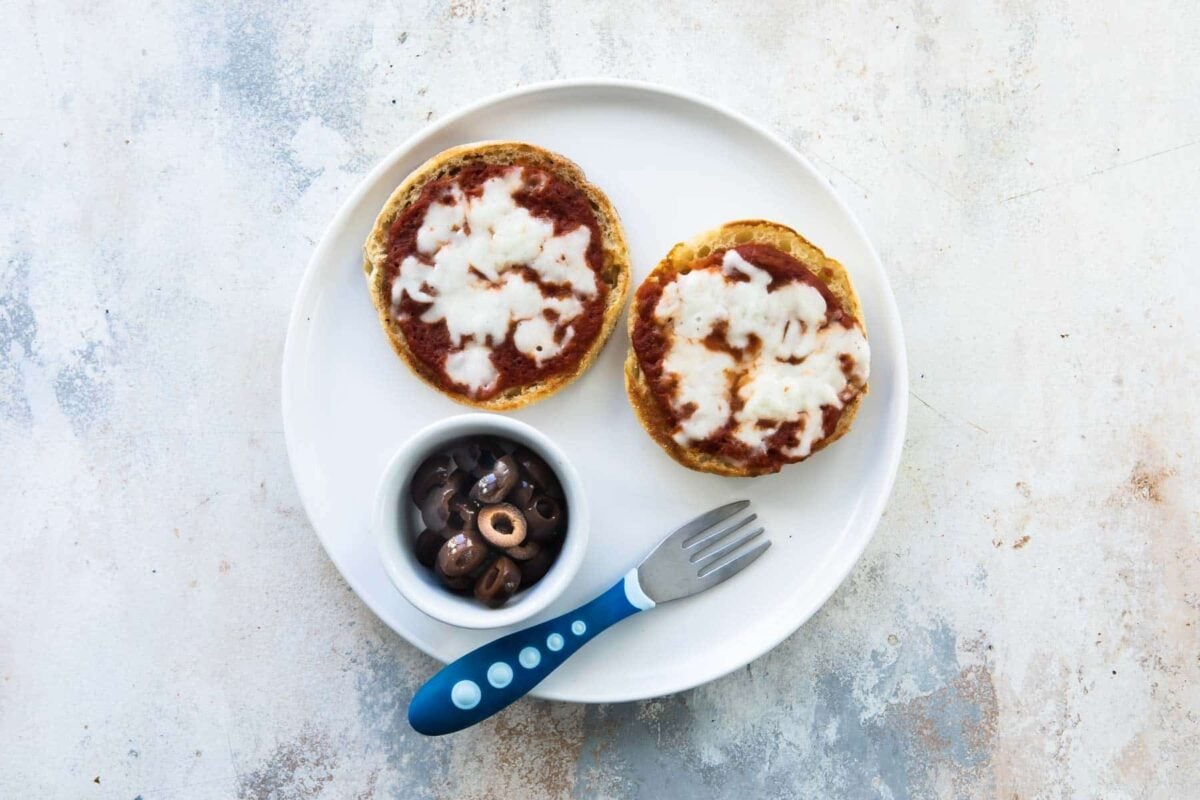 A toddler lunch of English muffin pizza with a side of olives.